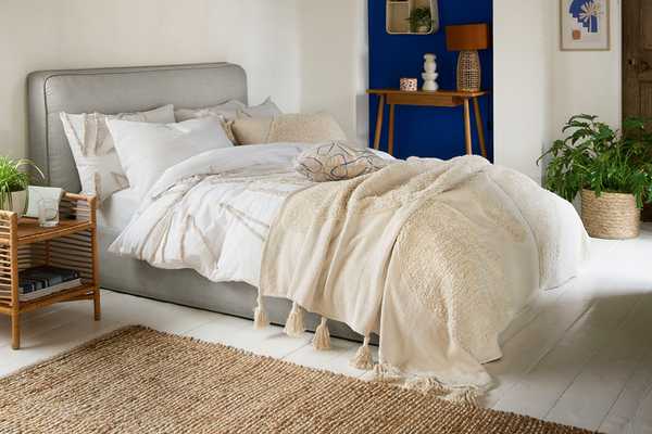 A mediterranean theme bedroom with a grey bed, white bedding, and all natural finish furniture. 